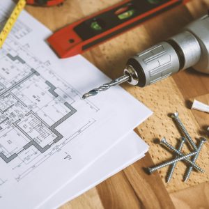 Close-up of construction blueprint with tools like drill and screws on a wooden table.